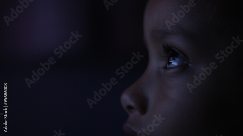 4K Close up of child's eyes watching a colourful screen in the dark