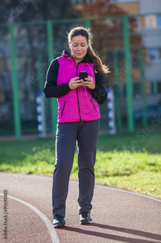Young woman messaging with mobile phone while standing a running track of the stadium