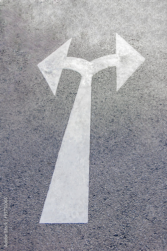 A two way arrow symbol on a black asphalt road surface.