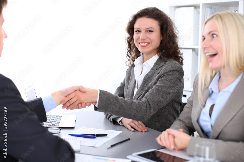 A group of business people at a meeting on the background of office. Focus on a beautiful brunette shaking hands A group of business people at a meeting on the background of office. Focus on a beautiful brunette shaking hands