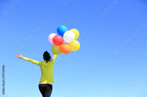cheering young woman running on mountain peak with colorful balloons © lzf
