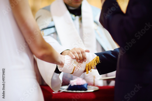 Canvas-taulu Bride and groom's hands wrapped in priest's cassock