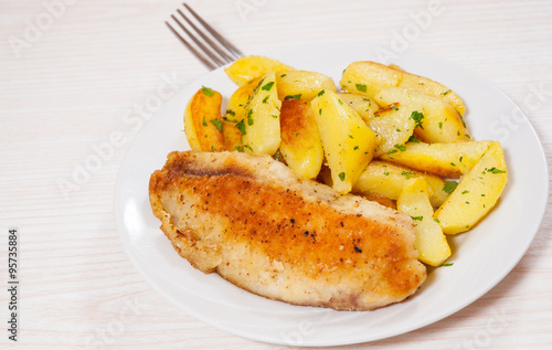 Fried fish fillet and potatoes in a plate
