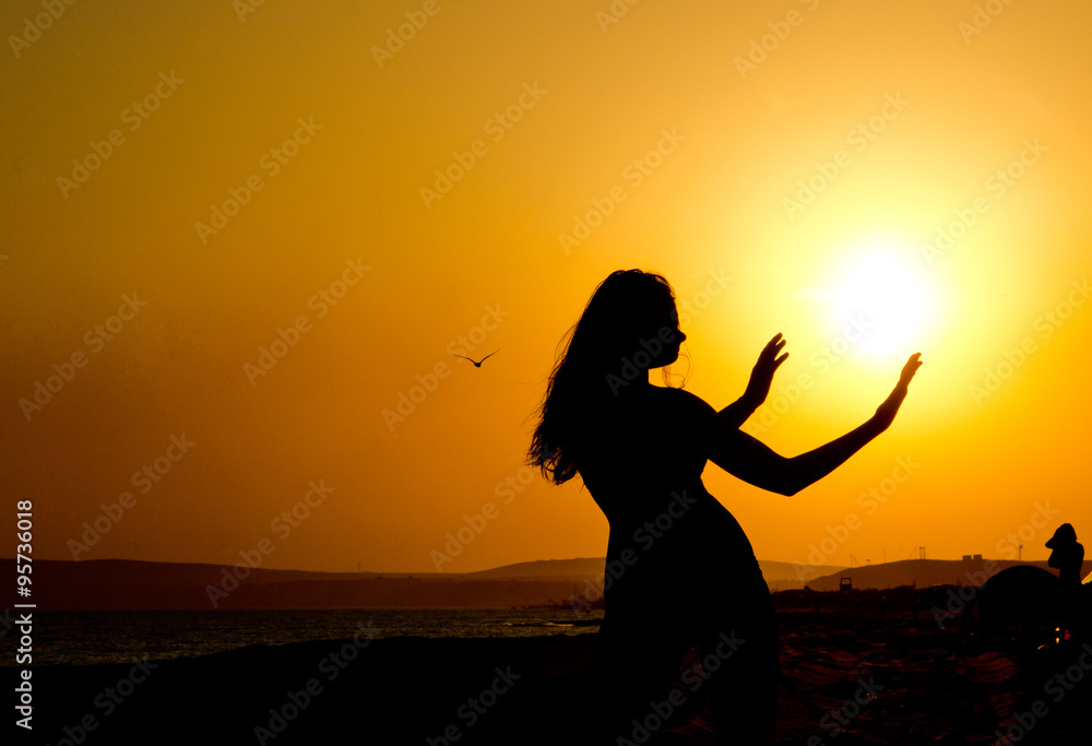 sleek silhouette of a girl with thin waist and hands outstretched to the sun at sunset