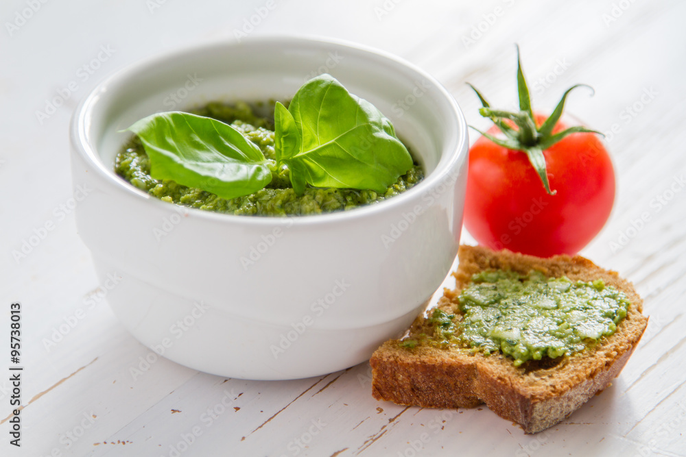 Pesto sauce in bowl, white wood background