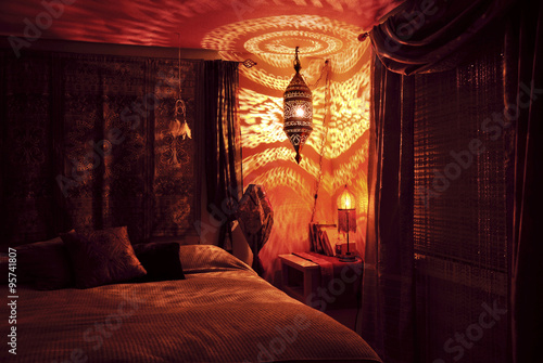 Moroccan bedroom with Moroccan lamp at night/Moroccan bedroom illuminated by Moroccan lamp with golden light pattern on wall