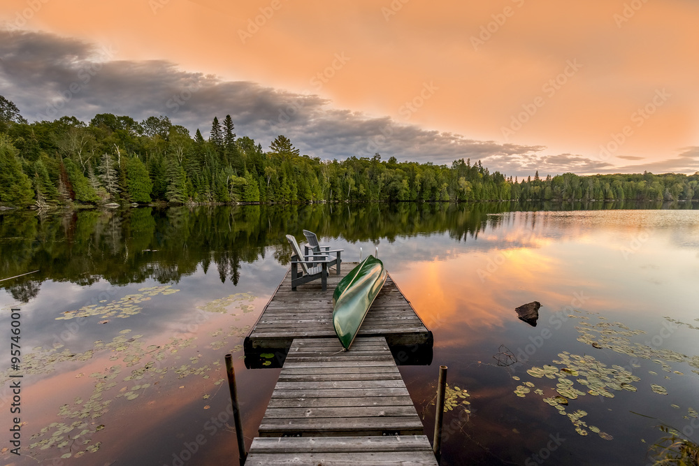 Obraz premium Green Canoe and Chairs on a Dock at Sunset