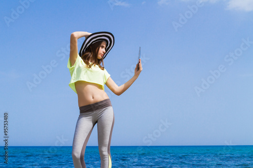 Beautiful teenage brunette using a tablet by the ocean.
