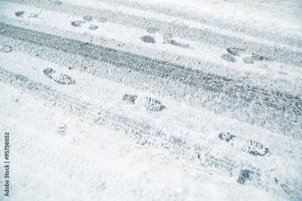 Snowy winter city asphalt road with tire trace and shoeprints. Danger icy and frozen city winter road background.