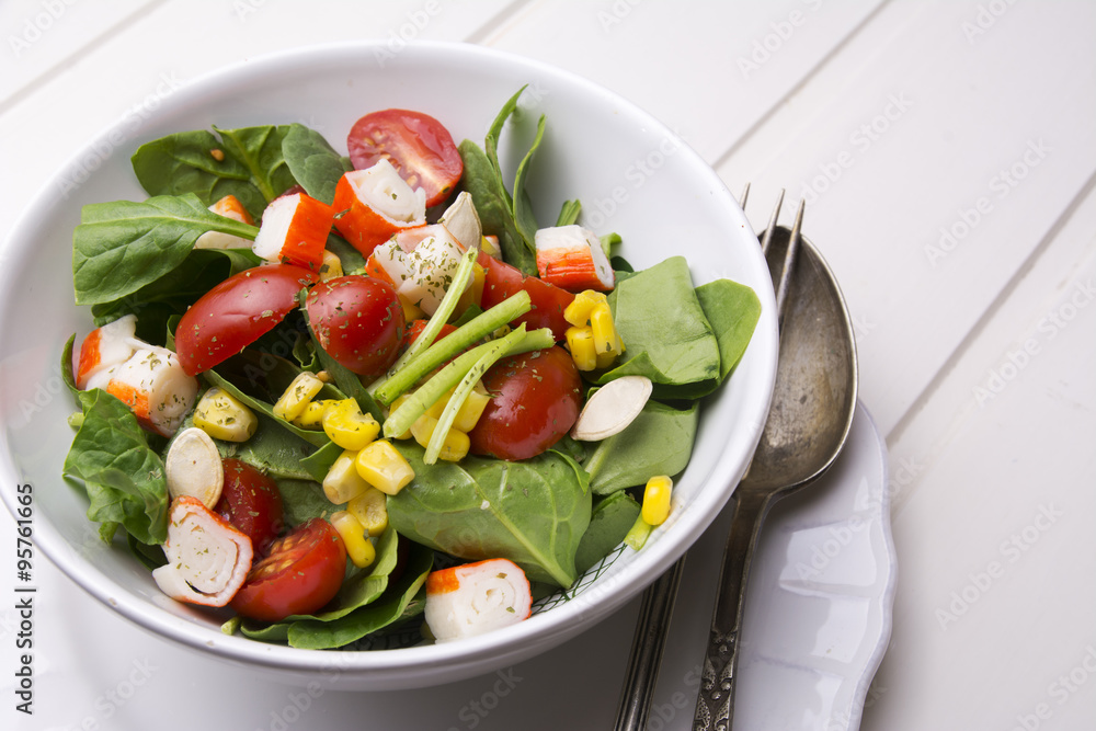 spinach salad with cherry tomatoes and corn in bowl, white wooden table
