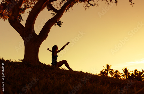 Silhouette of woman with hands raised into sunset