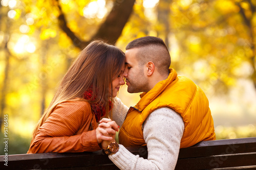 Young couple sitting on a park bench on a sunny autumn day and expressing tenderness