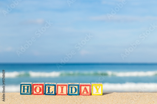 word HOLIDAY in colorful alphabet blocks on tropical beach