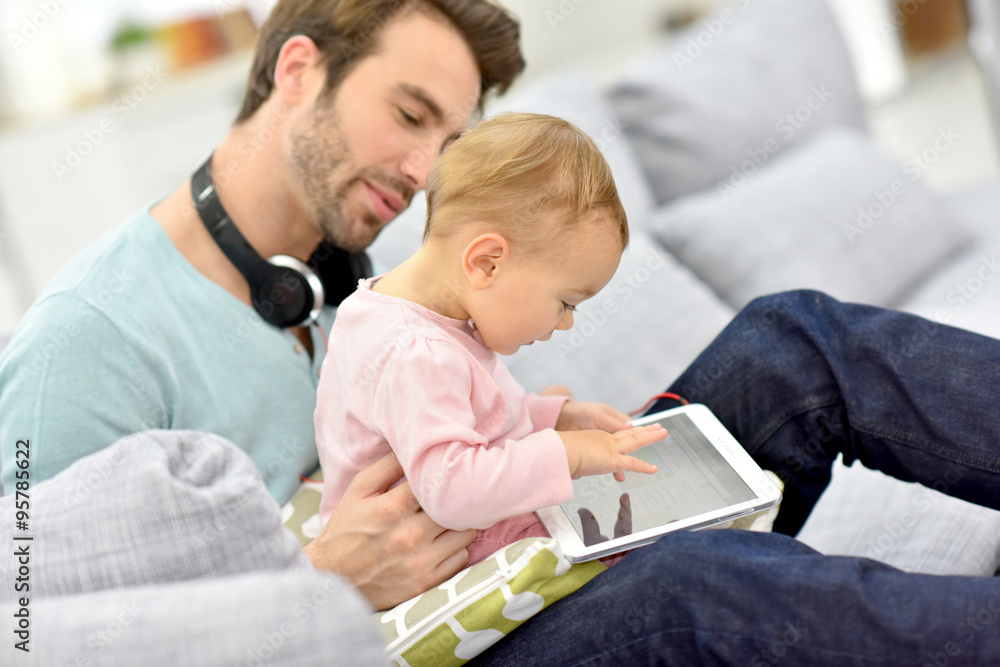Obraz premium Daddy and baby girl in sofa using tablet and headphones