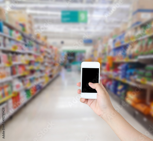 hand holding mobile phone with supermarket shelves aisle blurred