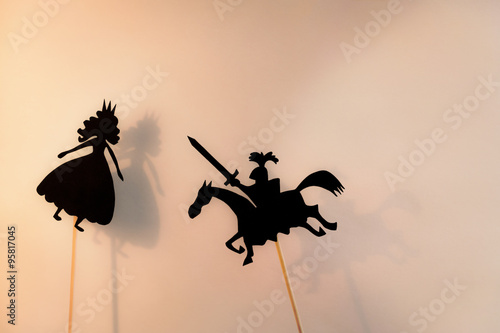 Shadow puppets of Princess and Knight and their shadows on the bright glowing screen of shadow theatre. Copy space background.