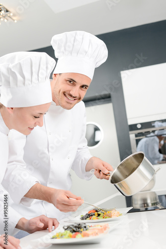 student and teacher in a professional cook school kitchen preparing a plate for restaurant