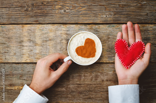 Men's hands hold cup of coffee and a toy heart for Valentine's D