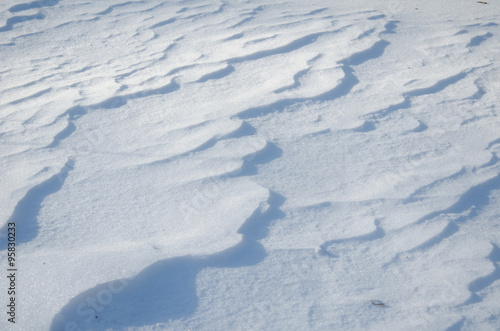 A blanket of snow, with soft ripples and ridges casting gentle shadows under a bright light. 