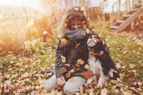 happy child girl playing with her dog on cozy outdoor walk, dropping leaves