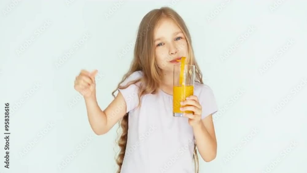 Girl drinking orange juice and dancing and smiling at camera. Girl with beautiful blonde hair on a white background. Thumb up. Ok Girl drinking orange juice and dancing and smiling at camera. Girl with beautiful blonde hair on a white background. Thumb up. Ok
