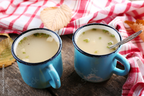 Two mugs of soup and napkin on wooden background
