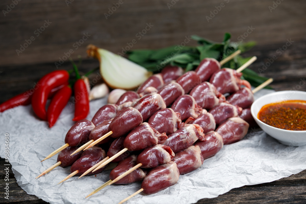 Ready to cook Duck Heart stringed on skewers BBQ , chili pepper. decorated with greens and vegetables. background