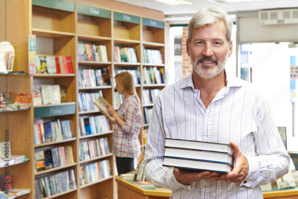 Portrait Of Male Bookstore Owner With Customer In Background Portrait Of Male Bookstore Owner With Customer In Background