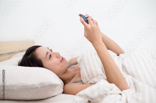 Woman lying down on bed and playing with the mobile phone