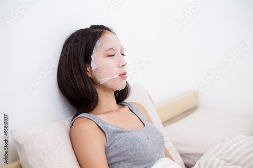 Woman sitting on bed and using the paper mask
