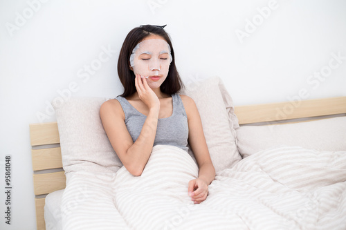Asian Woman sitting on bed and using the facial mask