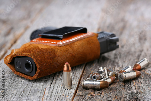 Photography Automatic Handgun with leather holster and bullets on a wooden background