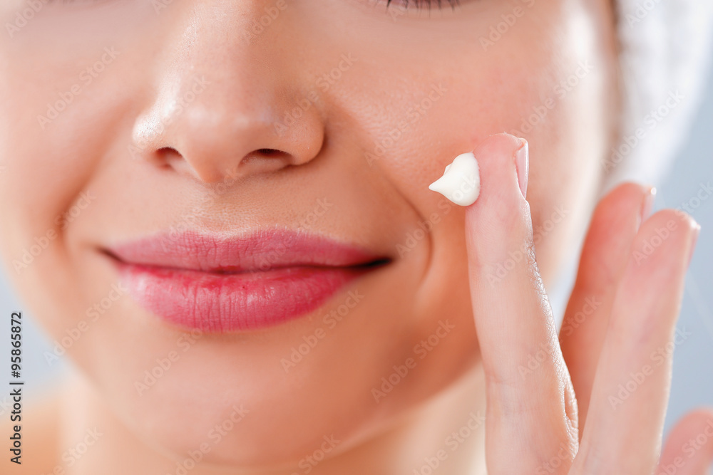 Beautiful young woman applying a creme on her face isolated on gray background Beautiful young woman applying a creme on her face isolated on gray background