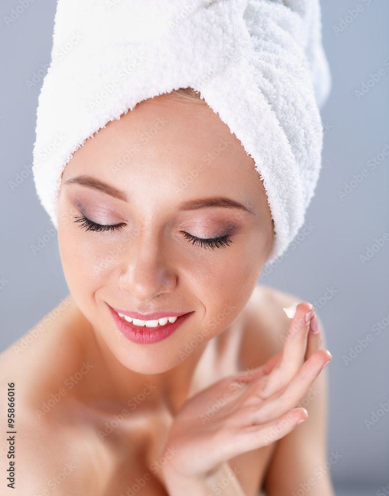 Beautiful young woman applying a creme on her face isolated on gray background Beautiful young woman applying a creme on her face isolated on gray background