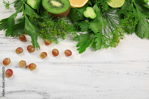 Cute bouquet of parsley and dill decorated with kiwi, lemons and cucumbers on light wooden background, close up