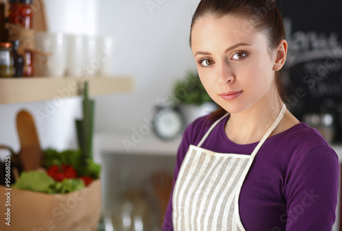 Young woman standing in her kitchen near desk with shopping bags