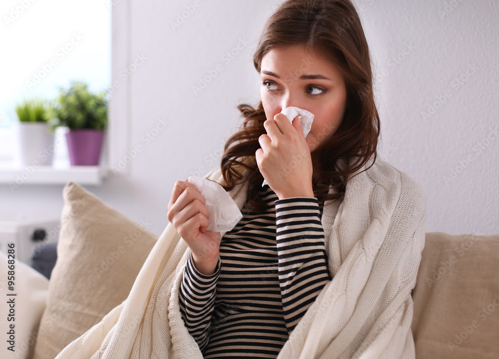 Portrait of a sick woman blowing her nose while sitting on the sofa Portrait of a sick woman blowing her nose while sitting on the sofa
