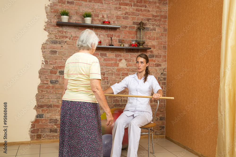 Fototapeta premium Physical Therapist Showing Exercise With A Stick For Senior Woman