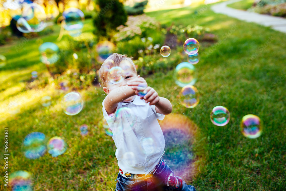 Little boy with soap bubbles in summer park.