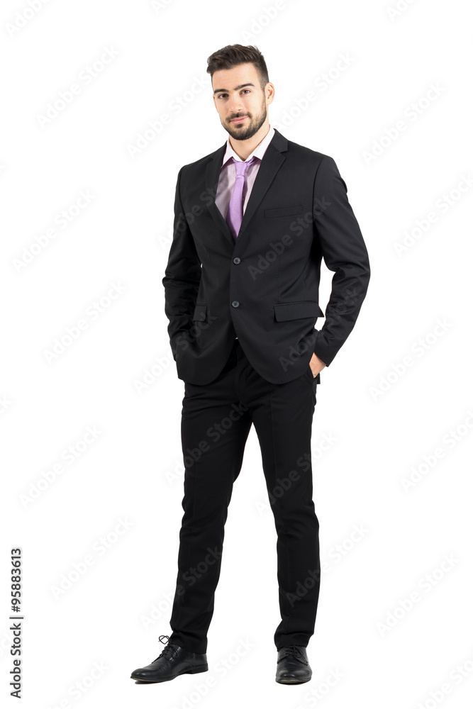 Confident young stylish man in suit looking at camera with hands in pockets. Full body length portrait isolated over white studio background. Confident young stylish man in suit looking at camera with hands in pockets. Full body length portrait isolated over white studio background.
