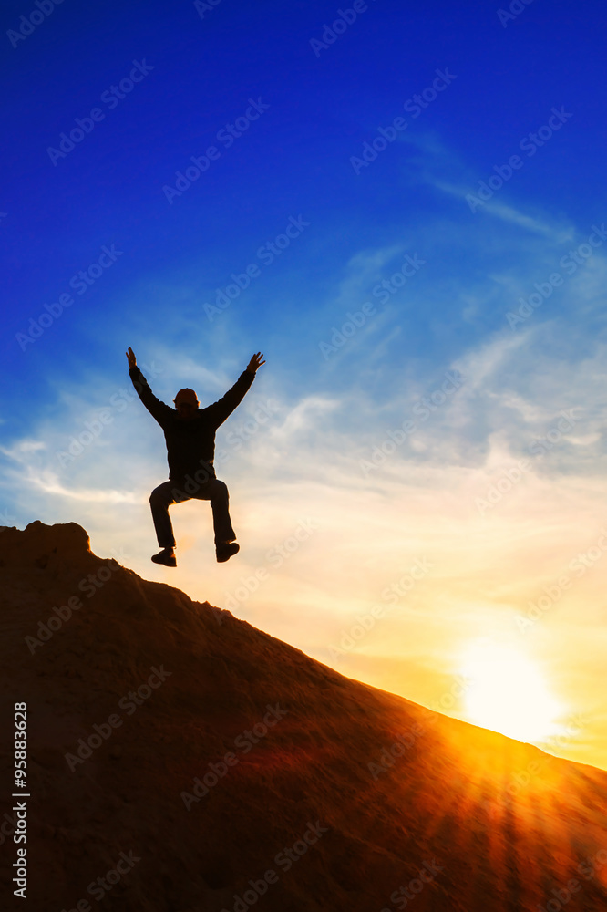 man jumping over a mountain at sunset