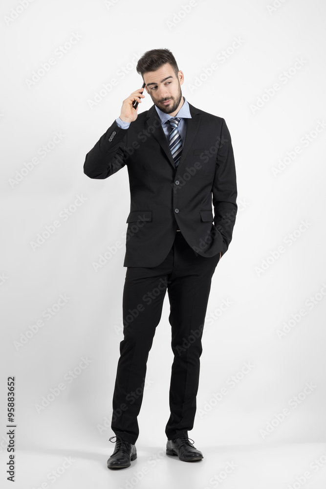 Cool young business man on the phone looking away. Full body length portrait over gray studio background. Cool young business man on the phone looking away. Full body length portrait over gray studio background.
