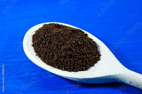 Ground coffee on wooden spoon on blue background photo