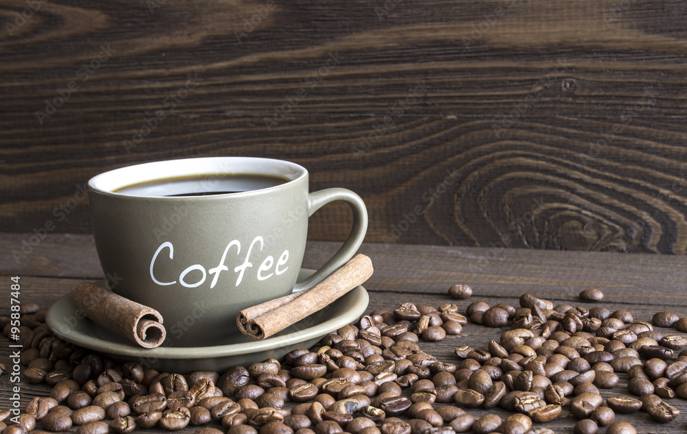 A cup of coffee, coffee beans and cinnamon sticks bark lying on an old wooden table A cup of coffee, coffee beans and cinnamon sticks bark lying on an old wooden table