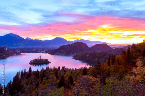 Lake Bled with small island and strong bright sunrise with bright sky and colorful trees in autumn, Bled, Slovenia, Europe