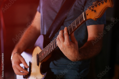 Young man playing on electric guitar close up