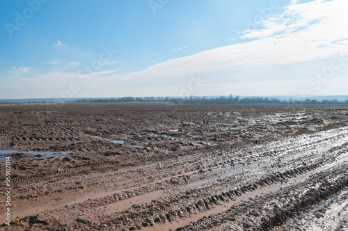 Vanishing dirty road through fallow field with mud and puddles at early spring
