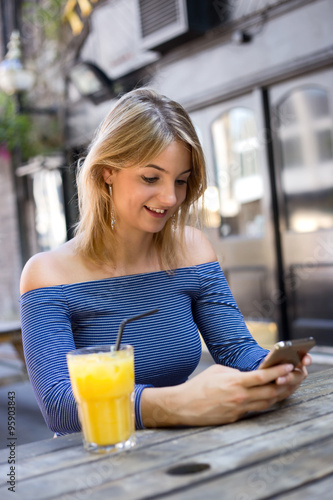 young woman sitting outside a bar with a orange juice and phone