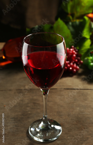 Red wine glass against wicker basket with grape and wine bottle on wooden table