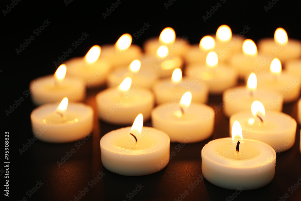 Alight candles in a row on black background, blurred